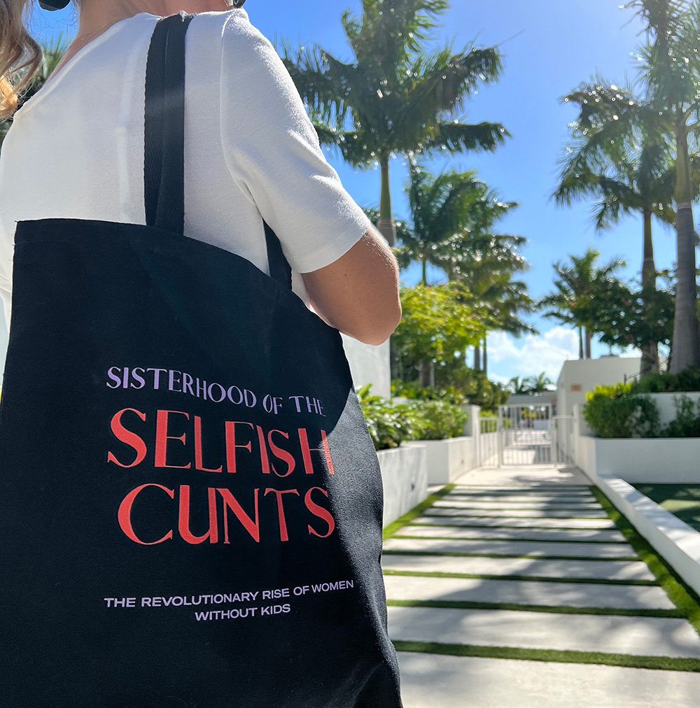 women wearing black color tote bag that reads: sisterhood of selfish c*nts the revolutionary rise of women without kids
