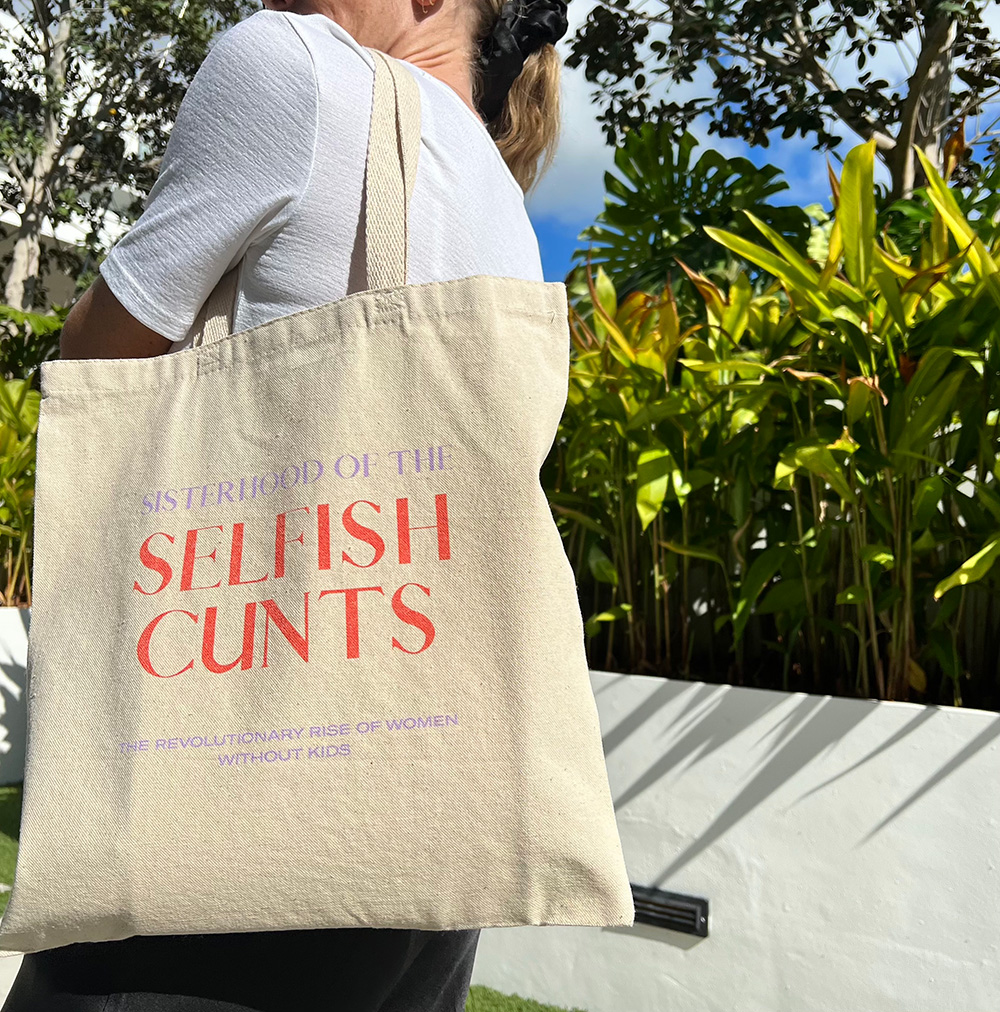 women wearing natural color tote bag that reads: sisterhood of selfish c*nts the revolutionary rise of women without kids